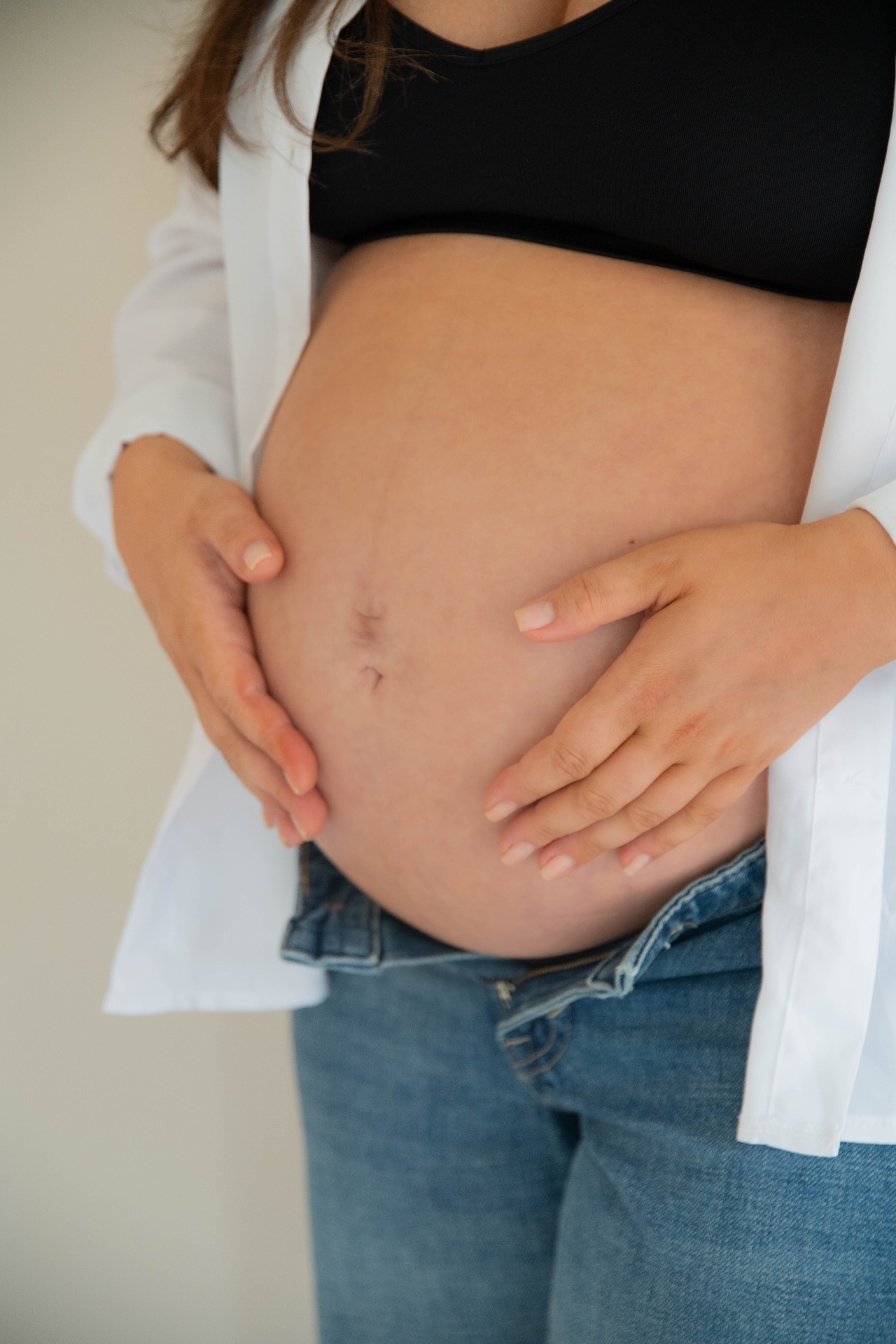 Close maternity detail of hands resting on a bump above denim