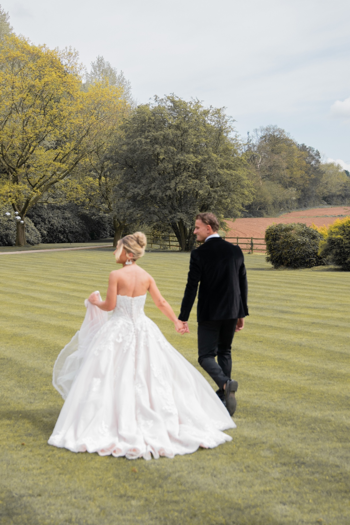Bride and groom walking hand in hand across a manor lawn