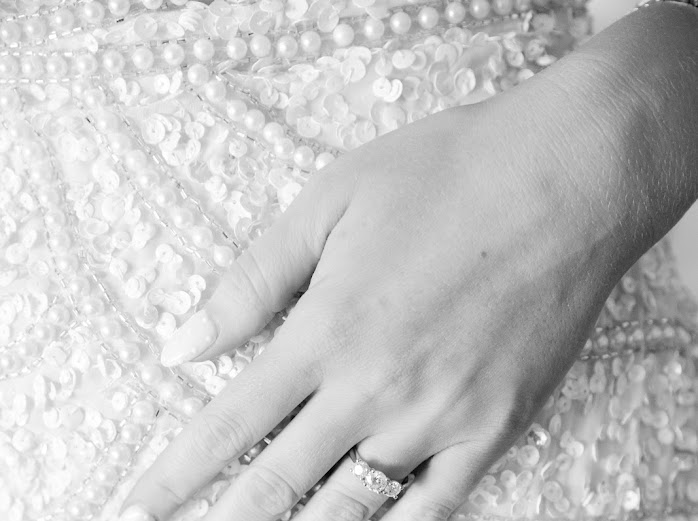 Black and white detail of an engagement ring resting on a beaded gown