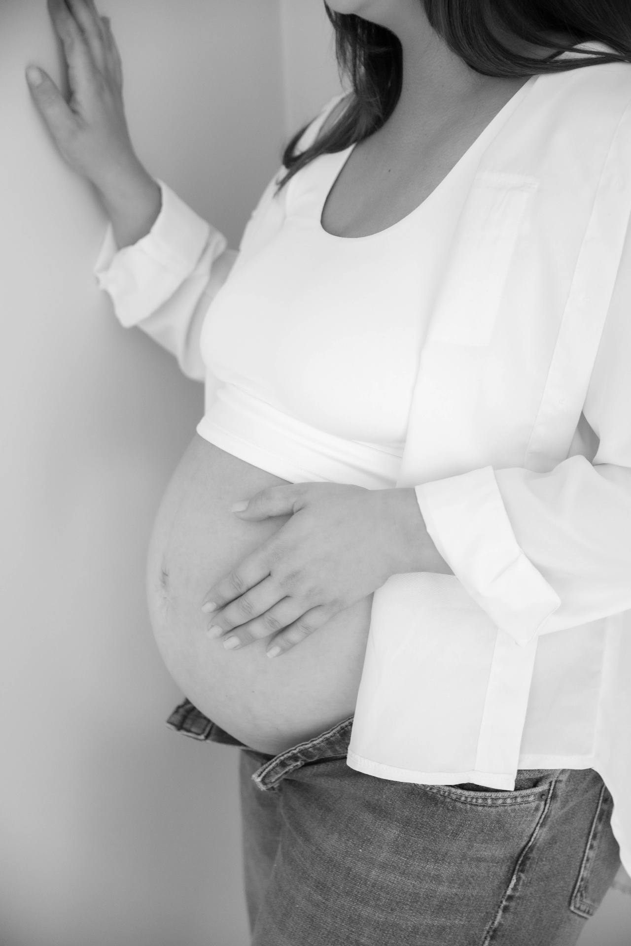 Black and white maternity portrait with one hand resting on the wall