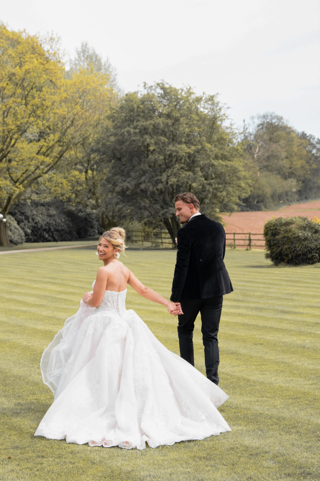 Bride and groom holding hands walking across a manor lawn