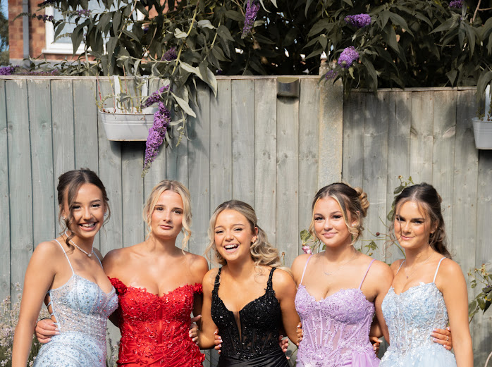 Group of friends in prom dresses laughing together in a garden