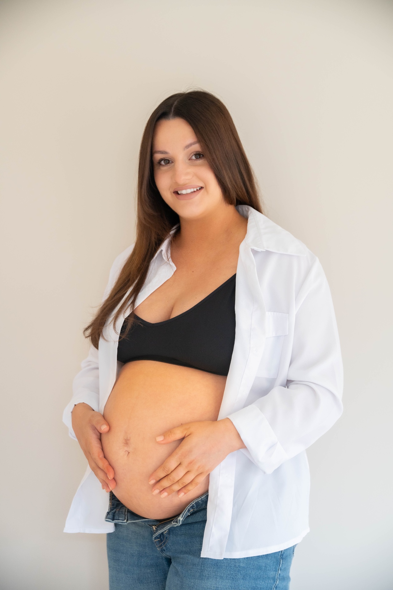 Expectant mother in a white shirt smiling and holding her bump