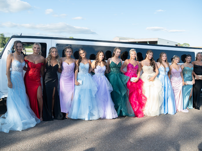 Group of friends in prom dresses beside a white limousine